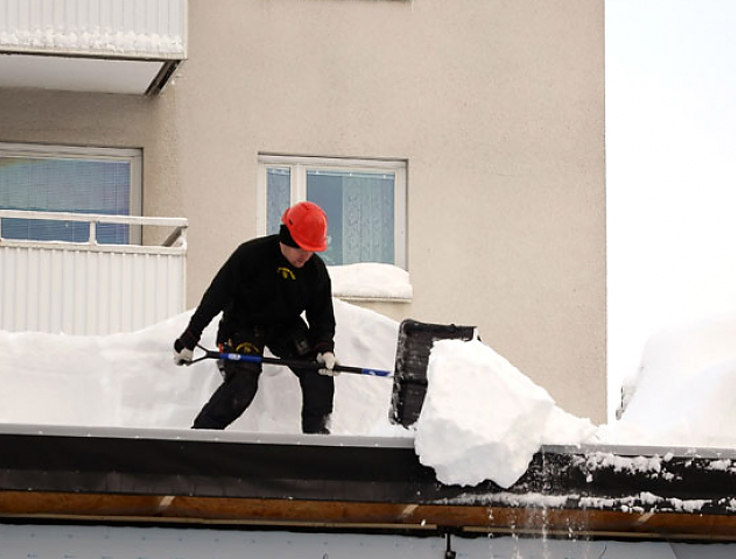 Bild man som skottar snö från tak