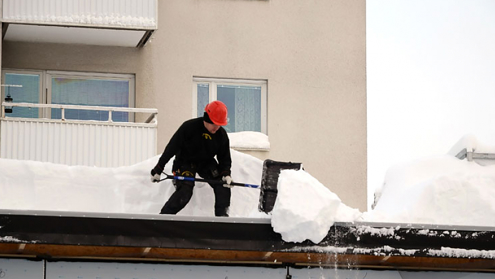 Bild man som skottar snö från tak